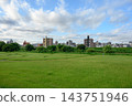 廣闊的綠色草原延伸到藍天之上，遠處可見公寓大樓和城市景觀——這是一片開闊的郊區景觀。 143751946