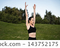 Individual performs a yoga pose in a tranquil park surrounded by greenery 143752175