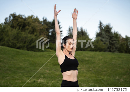 Individual performs a yoga pose in a tranquil park surrounded by greenery 143752175