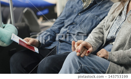 Close up of senior man and woman holding hands in airport lounge, chatting about ideas and future travel plans. Mature travelers sharing romantic moment before flight departure. Close up of senior man and woman holding hands in airport lounge, chatting about ideas and future travel plans. Mature travelers sharing romantic moment before flight departure. 143753199