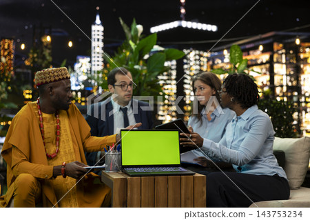 Green screen, laptop and business team as colleagues discuss paperwork behind blank chroma display on table. Screen replacement, collaboration and planning support mockup in rooftop lounge at night. 143753234