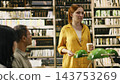 Student tutor, library discussion and coffee accompany woman in yellow speaking to classmates. Mentoring, peer learning and collaboration support group study around books and desk lamps. 143753269