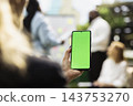 Green screen, mobile phone and display as woman shows blank smartphone with team behind her. Screen replacement, advertising and branding allow digital promotion in outdoor business workspace. 143753270