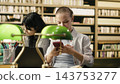Student, smartphone and laptop share attention as woman checks her phone beside study materials in the library. Distraction, screen time and study breaks illustrate challenges to academic focus. 143753277