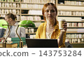 Coffee, laptop and student as red-haired woman raises a takeaway cup while pausing at her computer. Study break, refreshment and campus routine connect coursework with a brief rest in a library. 143753284