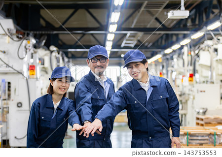 在製造廠裡,三名日本工人(兩男一女)面帶微笑,手牽手,表示團結一致。 在製造廠裡,三名日本工人(兩男一女)面帶微笑,手牽手,表示團結一致。 143753553