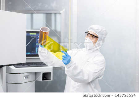 身穿潔淨服的工人在半導體製造廠對黃色醯亞胺薄膜的品質進行目視檢查。 身穿潔淨服的工人在半導體製造廠對黃色醯亞胺薄膜的品質進行目視檢查。 143753554
