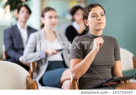 Young girl student dressed in business clothes sitting and listening lecture, taking notes on tablet in lecture hall Young girl student dressed in business clothes sitting and listening lecture, taking notes on tablet in lecture hall 143754397