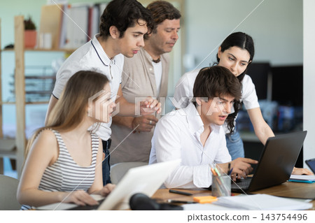 Colleagues looking at one laptop together in office Colleagues looking at one laptop together in office 143754496