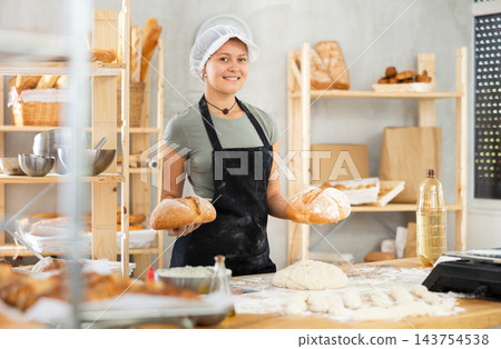 Young woman baker are standing near product range in bakery kitchen with basket of bread. Young woman baker are standing near product range in bakery kitchen with basket of bread. 143754538