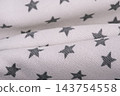 Knitted fabric of light beige color in gray stars. Macro photo of clothes as a background. 143754558