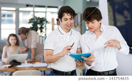 Two bank managers discuss documents in modern office Two bank managers discuss documents in modern office 143754635