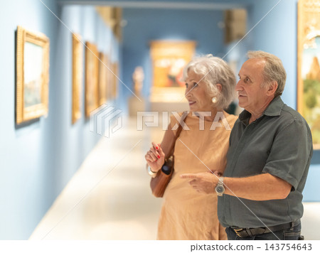 Senior couple looking at artistic pictures in foreground in museum Senior couple looking at artistic pictures in foreground in museum 143754643