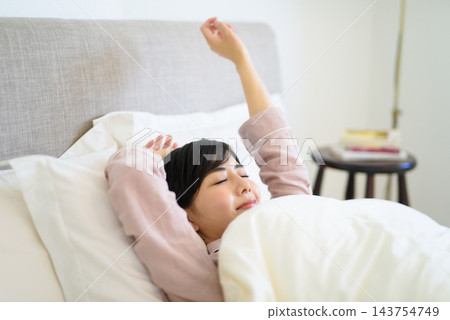 一位女士清晨醒來，在床上伸了個懶腰。 143754749