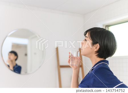 A woman drinking water from a glass in the bathroom. 143754752