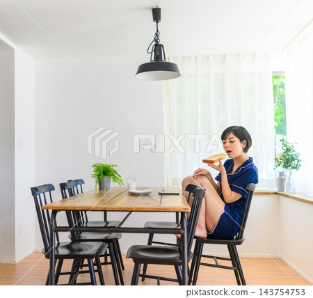 A woman in pajamas eating toast at the dining table. A woman in pajamas eating toast at the dining table. 143754753
