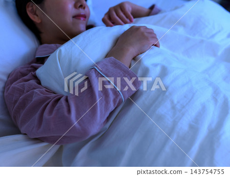 A woman sleeping wrapped in a blanket in her bedroom at night. A woman sleeping wrapped in a blanket in her bedroom at night. 143754755