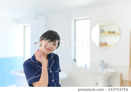 一位女士在浴室裡面帶著微笑，手裡拿著刮鬍刀。 143754758