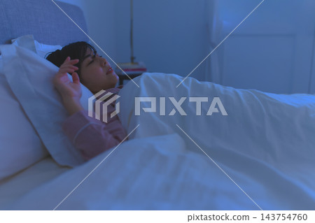 夜晚,一位女士躺在臥室的床上睡覺。 夜晚,一位女士躺在臥室的床上睡覺。 143754760