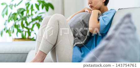 一位女士坐在沙發上,抱著靠墊,神情沮喪。 一位女士坐在沙發上,抱著靠墊,神情沮喪。 143754761