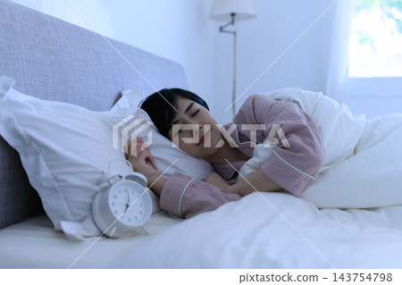 清晨,一位女士正在床上睡覺,這時鬧鐘響了。 清晨,一位女士正在床上睡覺,這時鬧鐘響了。 143754798