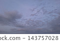 Scattered grey clouds drift across a soft purple and blue twilight sky at dusk 143757028