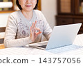 A middle-aged/senior woman making a circular pose while using her computer in her living room at home. 143757056