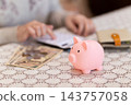 A middle-aged/senior woman counts her money in a pink piggy bank. 143757058