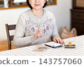 A middle-aged or senior woman holds up her index finger while calculating money on a calculator. 143757060