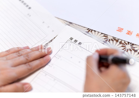 一位中老年女性在家裡的客廳寫履歷時的手。 143757148