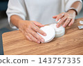 Close up of a senior asian woman's hands taking facial moisturizing cream from jar. 143757335