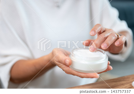 Close up of a woman's hands of senior woman touching moisturizer cream in jar. Close up of a woman's hands of senior woman touching moisturizer cream in jar. 143757337