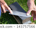 The hands of an old man sharpening a knife 143757566