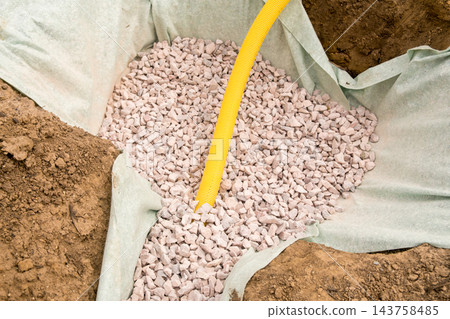 From a closeup perspective, granular stones are placed within landscaping fabric at a construction site. From a closeup perspective, granular stones are placed within landscaping fabric at a construction site. 143758485