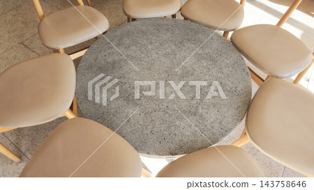 Round stone table surrounded by chairs in a dining area 143758646
