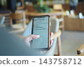 Person checks 2027 goals on a phone while seated in a cafe 143758712