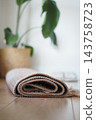 Rolled woven rug on a wooden floor beside a potted plant 143758723