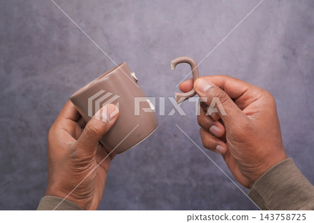 Hands hold a broken brown mug and its detached handle 143758725