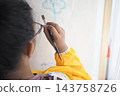 Child holding a paintbrush to draw a cloud on paper indoors 143758726
