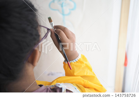 Child holding a paintbrush to draw a cloud on paper indoors 143758726