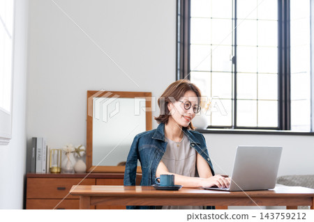 在客廳裡使用電腦的中年女人 在客廳裡使用電腦的中年女人 143759212