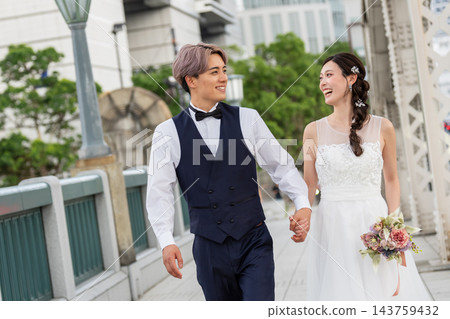 新郎新娘手牽手走過城市裡的一座橋。 143759432