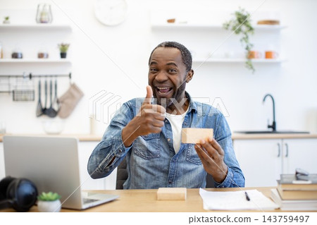 A laptop, papers, and a small kraft-colored parcel sit nearby, while open shelves, a sink, and soft daylight create a bright domestic setting A laptop, papers, and a small kraft-colored parcel sit nearby, while open shelves, a sink, and soft daylight create a bright domestic setting 143759497