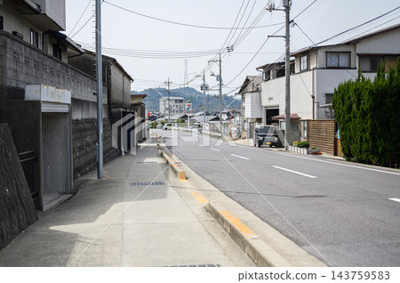 日本住宅區白天的寧靜街景,電線桿和電線沿著道路和人行道延伸,兩旁是獨立式住宅和老舊建築,遠處可以看到山脈。 日本住宅區白天的寧靜街景,電線桿和電線沿著道路和人行道延伸,兩旁是獨立式住宅和老舊建築,遠處可以看到山脈。 143759583