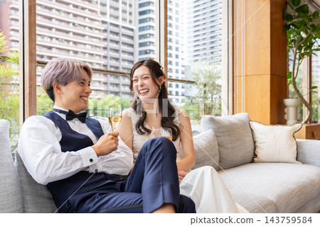一對笑容滿面的新婚夫婦在休息室的沙發上放鬆休息。 一對笑容滿面的新婚夫婦在休息室的沙發上放鬆休息。 143759584