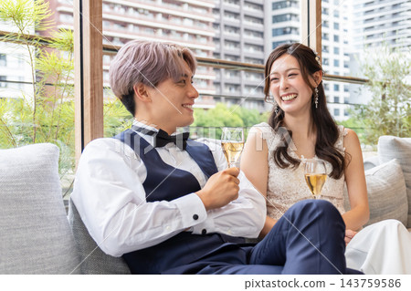 一對笑容滿面的新婚夫婦在休息室的沙發上放鬆休息。 一對笑容滿面的新婚夫婦在休息室的沙發上放鬆休息。 143759586