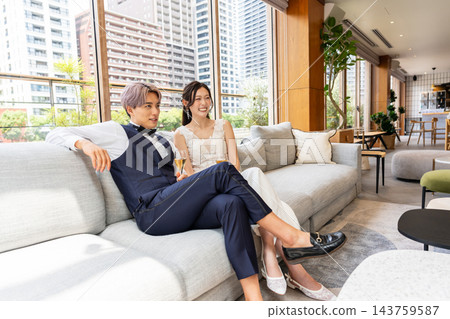 一對笑容滿面的新婚夫婦在休息室的沙發上放鬆休息。 143759587