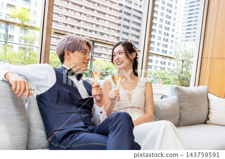 一對笑容滿面的新婚夫婦在休息室的沙發上放鬆休息。 一對笑容滿面的新婚夫婦在休息室的沙發上放鬆休息。 143759591