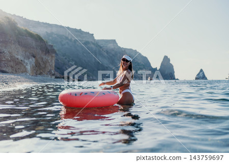 Woman, ocean, inflatable. Happy young woman floats on a pink donut ring in the clear sea near rocky cliffs. Woman, ocean, inflatable. Happy young woman floats on a pink donut ring in the clear sea near rocky cliffs. 143759697