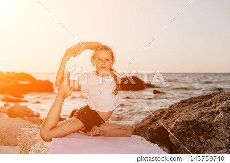 Flexible child practicing advanced yoga pose on rocky seashore during warm sunset light Flexible child practicing advanced yoga pose on rocky seashore during warm sunset light 143759740